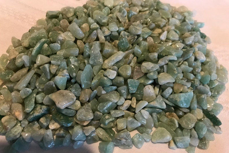 May include: A pile of small, light green and white tumbled stones. The stones are smooth and polished, and they have a natural, organic look.
