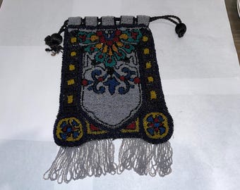 Puede incluir: Un bolso vintage de cuentas con un diseño floral en tonos azules, verdes, amarillos y rojos. El bolso tiene un cierre de cordón y un ribete de flecos.