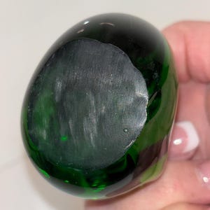 May include: A dark green glass paperweight with a smooth, rounded surface.