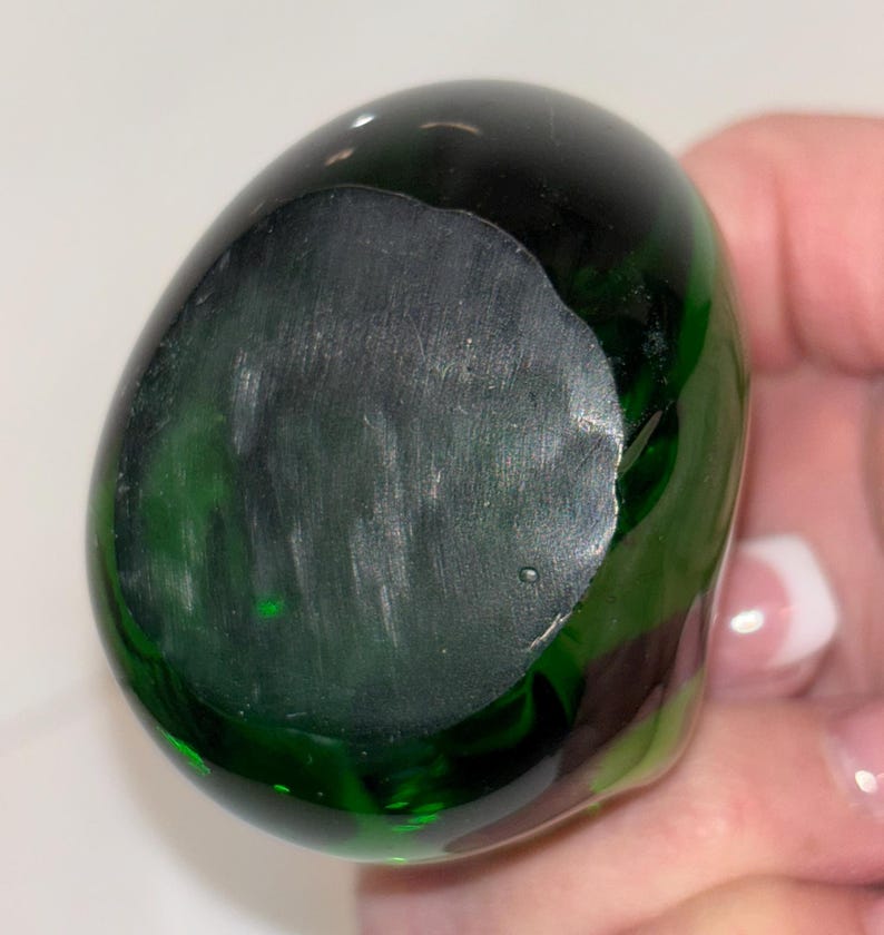 May include: A dark green glass paperweight with a smooth, rounded surface.