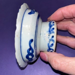 May include: A small, white ceramic bowl with a blue and white floral design. The bowl has a scalloped edge and a raised base.