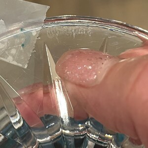 May include: Close-up of the bottom of a clear glass vase with a cut-glass design. The vase has a thick rim and a small amount of white residue on the bottom.