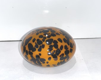 May include: An oval-shaped decorative object with a glossy finish. The object is primarily orange with irregular black spots, resembling a tortoise shell pattern. The design is symmetrical and the object is smooth.