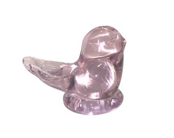 Peut inclure: Une figurine d'oiseau en verre translucide de couleur violet clair. L'oiseau est posé sur une base circulaire, les ailes légèrement déployées. Le verre a une surface lisse et réfléchissante.