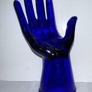 Peut inclure: Une sculpture de main en verre bleu cobalt avec une paume ouverte et une base &eacute;vas&eacute;e.