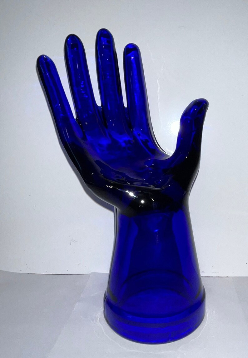 Peut inclure: Une sculpture de main en verre bleu cobalt avec une paume ouverte et une base &eacute;vas&eacute;e.