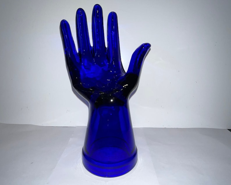 Peut inclure: Une sculpture de main en verre bleu cobalt. La main est lev&eacute;e, les doigts &eacute;cart&eacute;s. La main est fix&eacute;e &agrave; une base &eacute;galement en verre bleu cobalt.