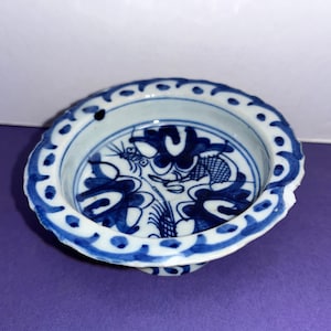 May include: A small, white porcelain bowl with a blue and white floral design. The bowl has a scalloped edge and a raised base.