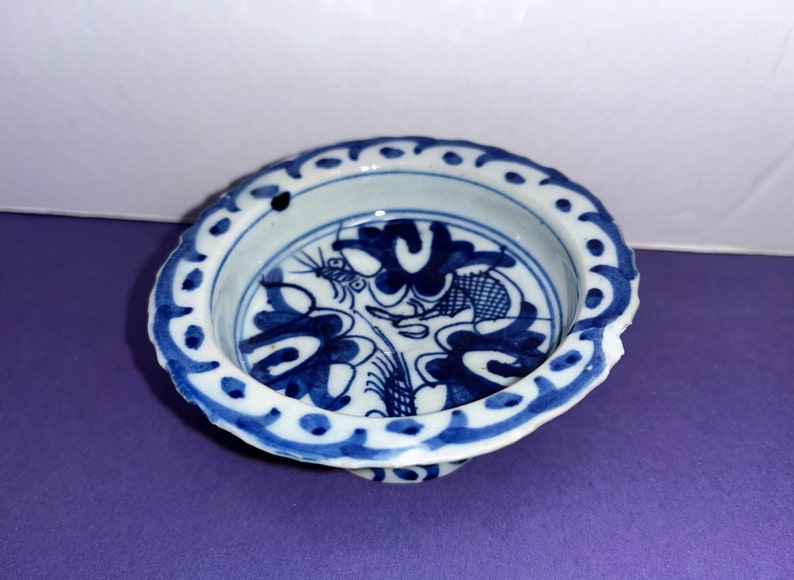 May include: A small, white porcelain bowl with a blue and white floral design. The bowl has a scalloped edge and a raised base.