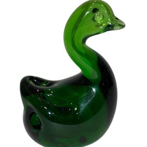 May include: A green glass duck figurine. The duck is sitting with its head turned to the side. The duck has a round body and a long neck.