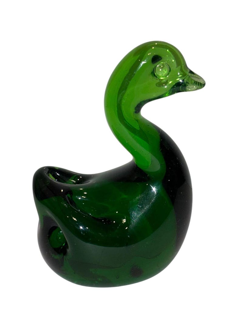 May include: A green glass duck figurine. The duck is sitting with its head turned to the side. The duck has a round body and a long neck.