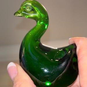 May include: A green glass swan figurine. The swan has a long neck and a rounded body. The glass is clear and shiny.