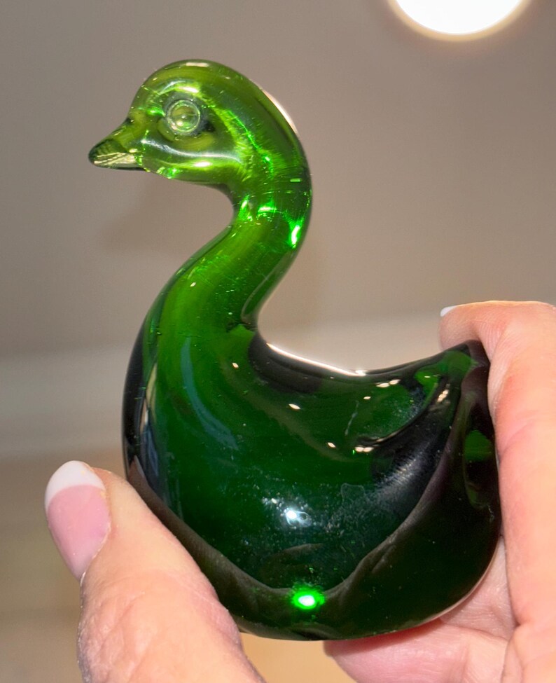 May include: A green glass swan figurine. The swan has a long neck and a rounded body. The glass is clear and shiny.