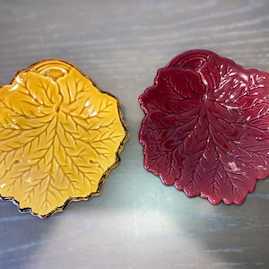 May include: Two ceramic leaf-shaped serving dishes. One is yellow and the other is red.