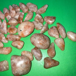 May include: A collection of sunstone tumbled stones in various sizes and shapes. The stones are a light orange color with a shimmery, iridescent finish.