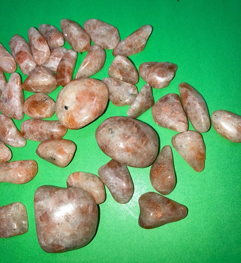 May include: A collection of sunstone tumbled stones in various sizes and shapes. The stones are a light orange color with a shimmery, iridescent finish.