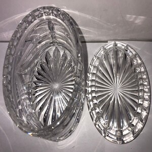 May include: A clear glass oval-shaped box with a lid. The box and lid have a cut-glass design with a starburst pattern.