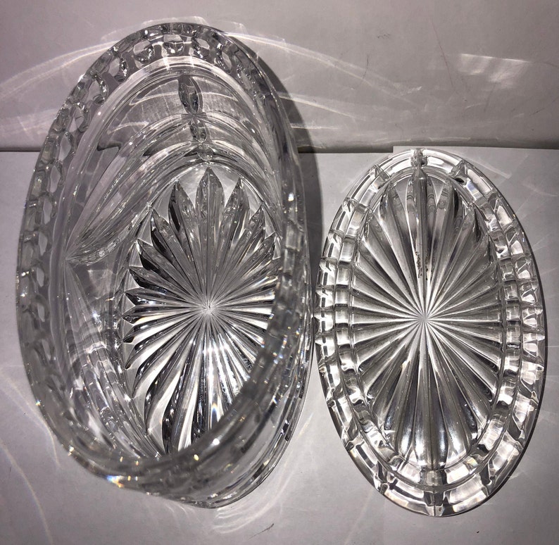 May include: A clear glass oval-shaped box with a lid. The box and lid have a cut-glass design with a starburst pattern.