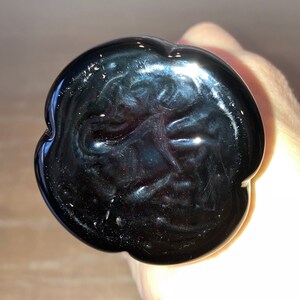 May include: Black glass bottle stopper with a unique, swirling design. The stopper is shaped like a flower with a smooth, glossy finish.