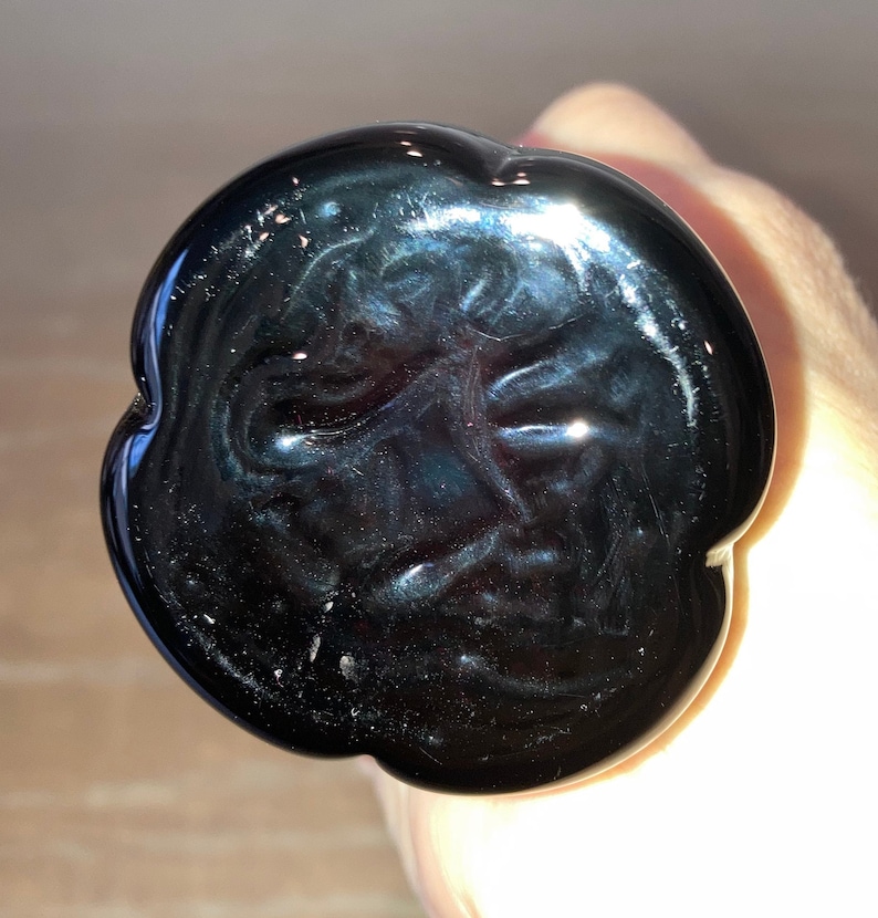 May include: Black glass bottle stopper with a unique, swirling design. The stopper is shaped like a flower with a smooth, glossy finish.