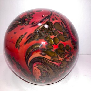 Può includere: Una sfera di vetro rossa, nera e dorata con motivi a spirale e scaglie dorate incorporate.