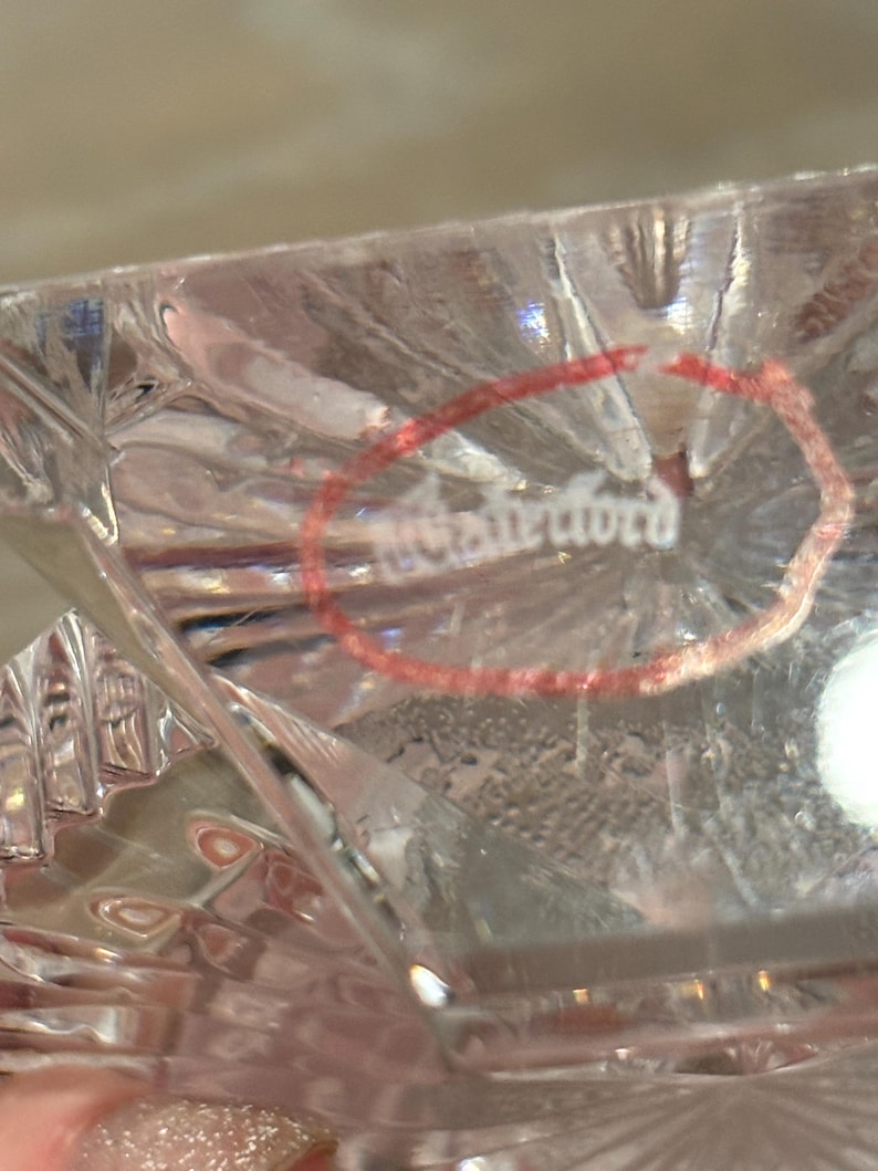 K&ouml;nnte beinhalten: Nahaufnahme eines klaren Kristallglases mit Diamantschliffmuster. Das Wort "Waterford" ist in einem roten Kreis sichtbar. Das Glas hat eine reflektierende Oberfl&auml;che.