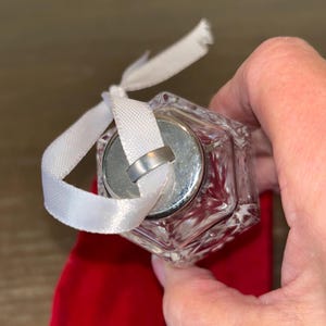 May include: A clear glass ornament with a silver top and a white ribbon. The ornament is shaped like a cube and has a textured surface.