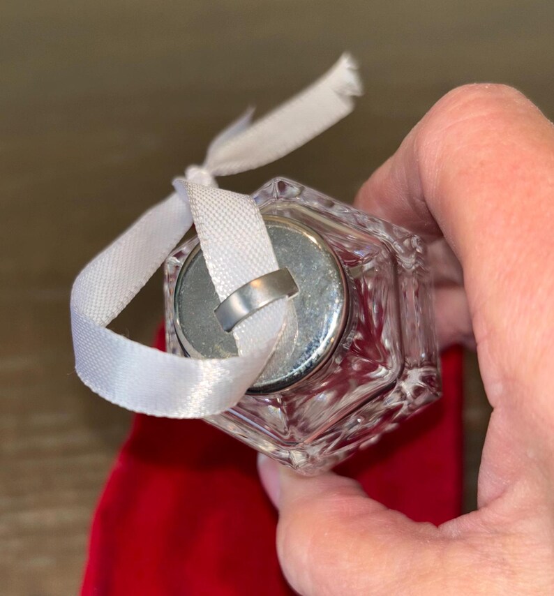 May include: A clear glass ornament with a silver top and a white ribbon. The ornament is shaped like a cube and has a textured surface.