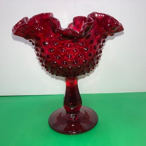 Op de afbeelding: Een rode glazen snoepkom met een gekrulde rand en een voet. De kom is bedekt met kleine, verhoogde stippen.