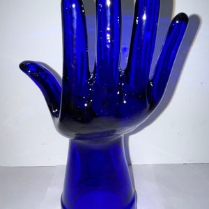 Peut inclure: Une sculpture de main en verre bleu cobalt avec une base arrondie. La main est lev&eacute;e, les doigts &eacute;cart&eacute;s.