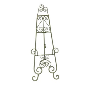 May include: A decorative metal easel in a muted gold color. The easel features ornate scrollwork and a three-legged base. The top has a decorative flourish, and the easel is designed to hold a picture or artwork.