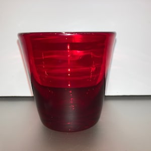 May include: A small, red glass cup with a ribbed design. The cup is empty and appears to be made of clear glass with a red tint.