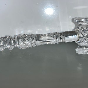 May include: A clear, cut-glass pipe with a hammer-shaped head and a diamond pattern. The pipe has a long, cylindrical stem with a decorative design. The overall design is ornate and elegant, with a focus on the intricate details of the glass.