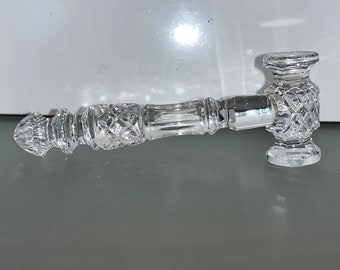 May include: A clear, cut-glass pipe with a hammer-shaped head and a diamond pattern. The pipe has a long, cylindrical stem with a decorative design. The overall design is ornate and elegant, with a focus on the intricate details of the glass.