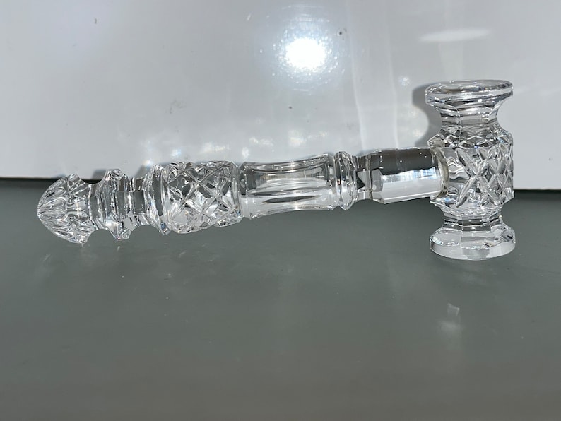 May include: A clear, cut-glass pipe with a hammer-shaped head and a diamond pattern. The pipe has a long, cylindrical stem with a decorative design. The overall design is ornate and elegant, with a focus on the intricate details of the glass.