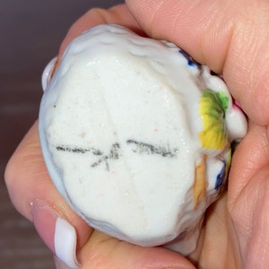 May include: A white porcelain figurine of a woman with a floral design. The figurine has a black inscription on the bottom that reads "Japan".