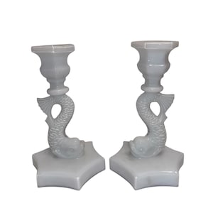 May include: A pair of light gray candle holders. Each holder features a dolphin design, with the dolphin's body forming the stem. The base is a four-pointed star shape. The top is a cup shape to hold a candle.
