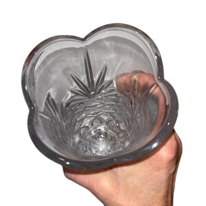 May include: Clear glass vase with a unique, scalloped rim. The interior features intricate starburst and geometric patterns. The vase is held by a hand, showcasing its elegant design. A decorative piece for floral arrangements or home decor.