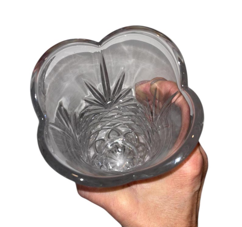 May include: Clear glass vase with a unique, scalloped rim. The interior features intricate starburst and geometric patterns. The vase is held by a hand, showcasing its elegant design. A decorative piece for floral arrangements or home decor.