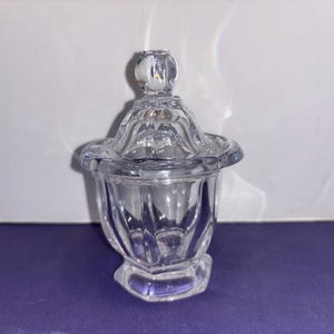 May include: A clear glass jar with a lid. The jar has a fluted design and a round base. The lid has a knob on top.