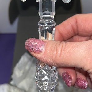 May include: A clear crystal gavel featuring intricate diamond-cut patterns on the handle and head. The head has a cylindrical shape with faceted ends, while the handle displays a multi-tiered, textured design with a pointed, decorative base.