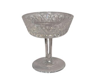May include: A clear, cut crystal champagne coupe glass. The bowl has a diamond pattern, and the stem is a slender, vertical design. The base is a flat, circular shape. The glass is designed for serving champagne or cocktails.