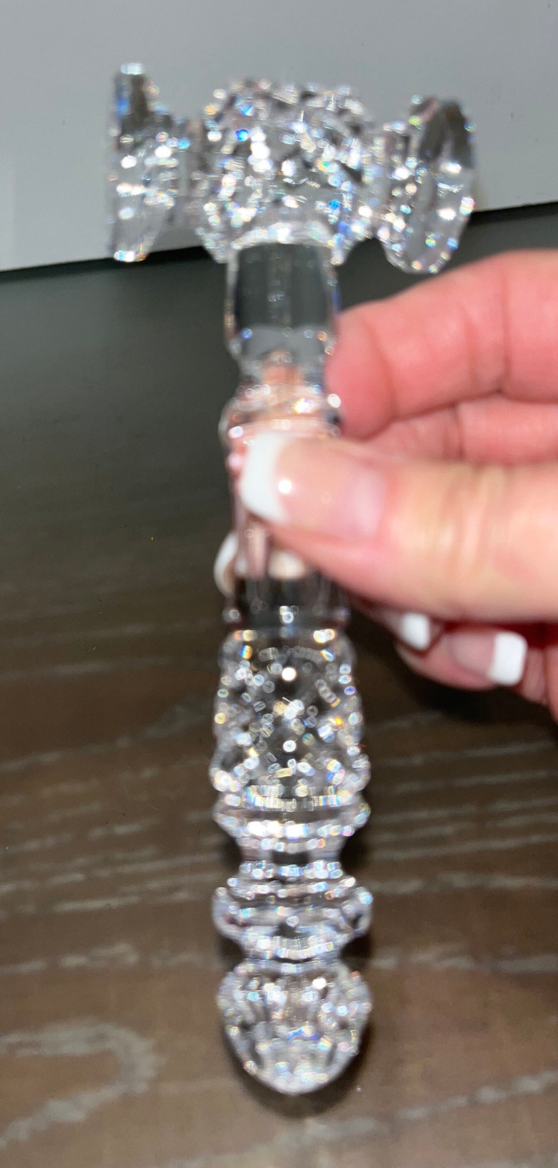 May include: A clear, crystal-like bottle stopper with a decorative, faceted design. The stopper has a cylindrical body and a flared top, all covered in sparkling, reflective facets. The overall effect is one of luxury and elegance.