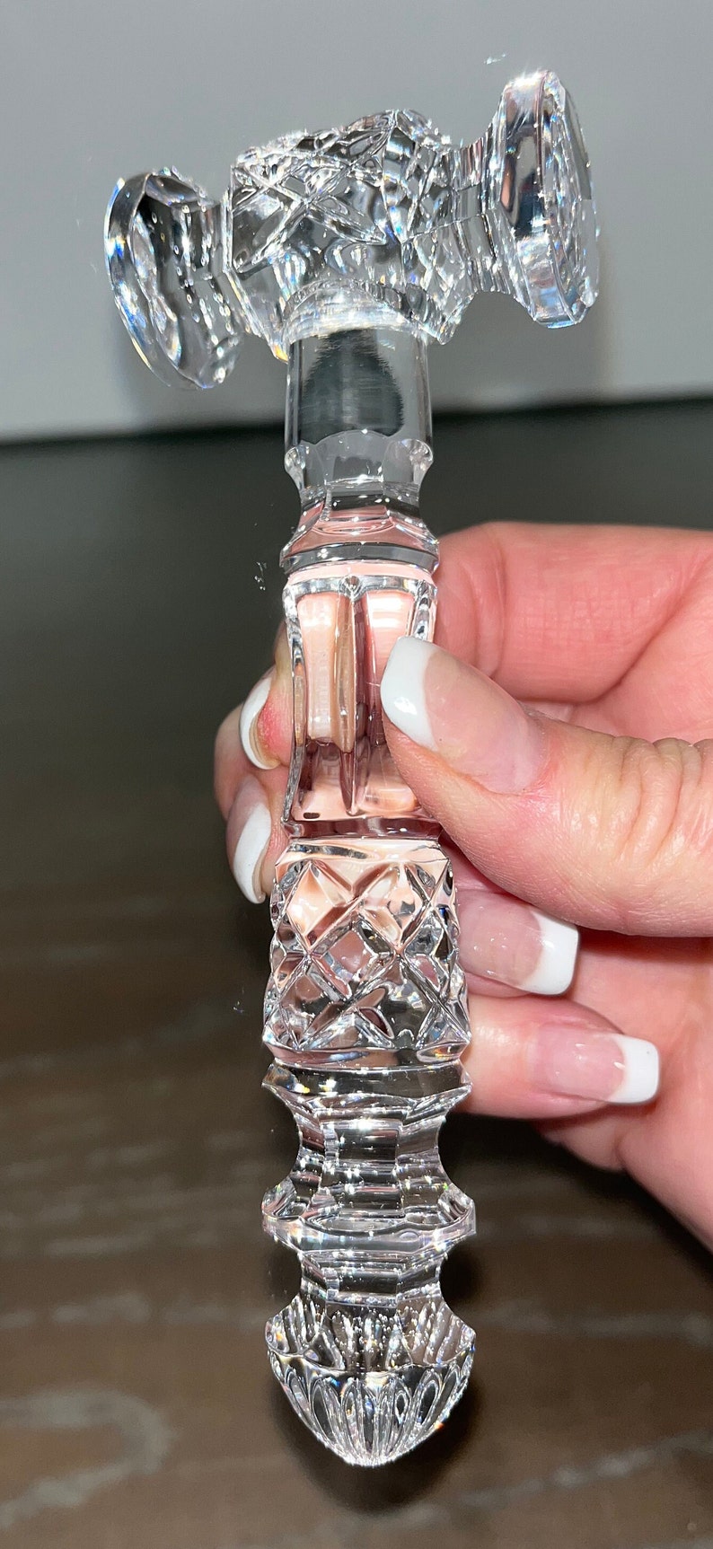 May include: A clear, faceted crystal bottle stopper with a decorative design. The stopper features a diamond-cut pattern and a cylindrical shape, perfect for wine bottles. The design is held by a hand.