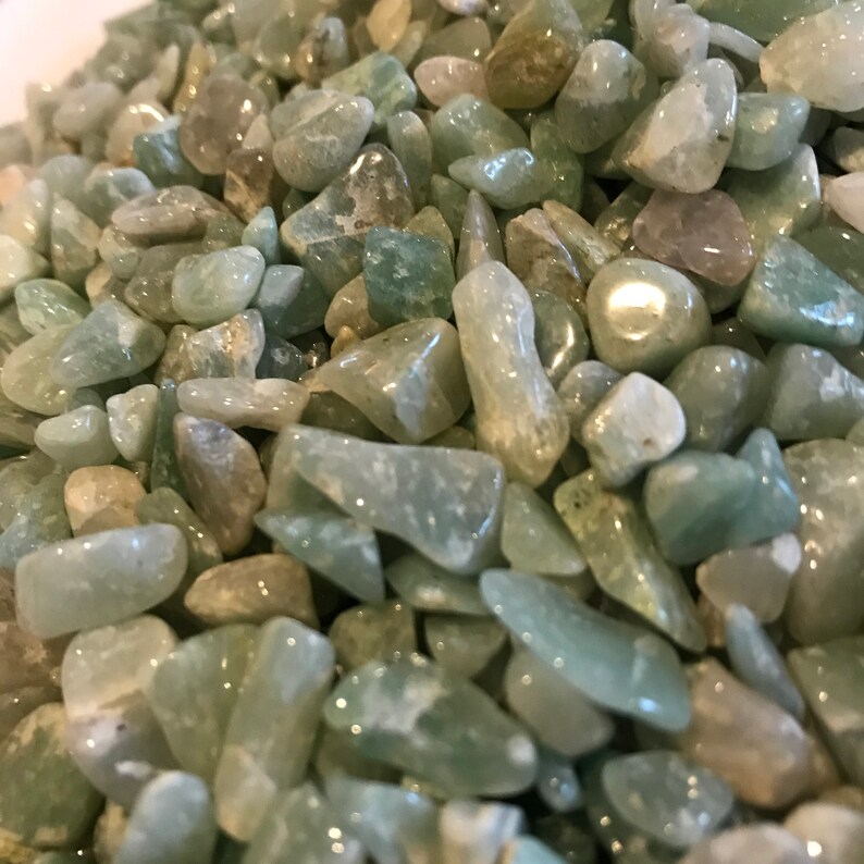 May include: A close-up of a pile of light green and white tumbled stones. The stones are smooth and polished, and they have a natural, organic look.