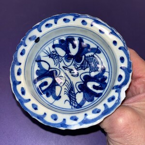May include: A small, white ceramic bowl with a blue and white floral design. The bowl has a scalloped edge and a raised rim.
