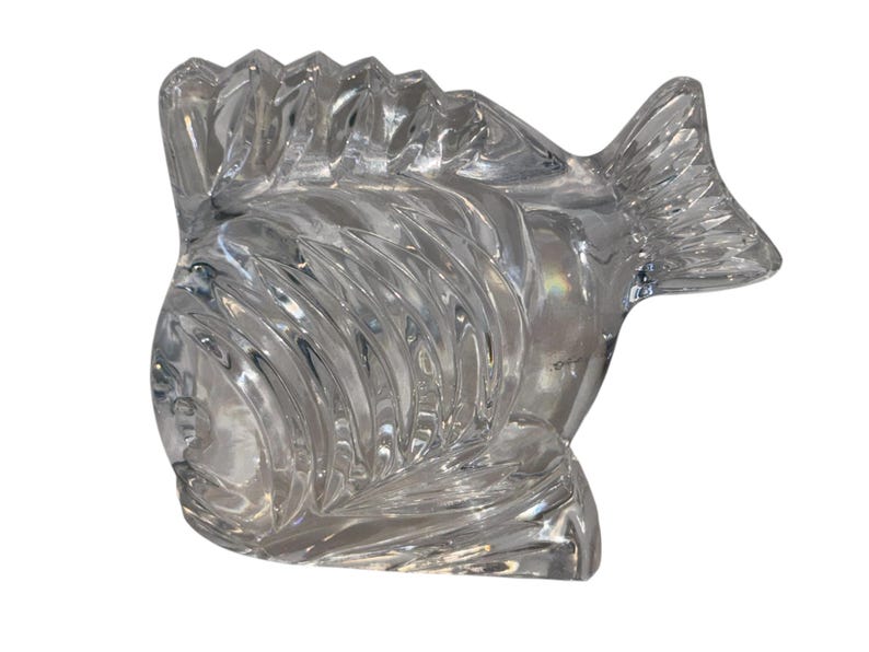 K&ouml;nnte beinhalten: Eine klare Fischskulptur aus Glas mit detaillierten, geschwungenen Linien. Der Fisch hat eine Flosse oben und eine Schwanzflosse. Die Skulptur ist transparent und reflektiert das Licht, wodurch ein schimmernder Effekt entsteht. Es ist ein dekorativer Gegenstand.