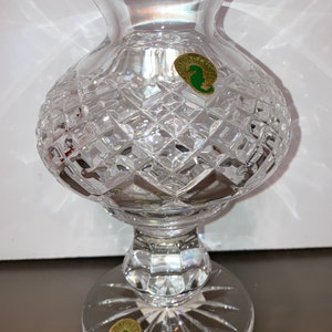 May include: A clear crystal vase with a cut glass design. The vase has a round body and a pedestal base. The vase has two labels on the bottom that say "Waterford Crystal" with a seahorse logo.