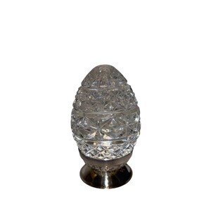 K&ouml;nnte beinhalten: Ein klarer, facettierter, dekorativer, eif&ouml;rmiger Gegenstand aus Glas mit silberfarbenem Sockel. Das Glas hat ein rautenf&ouml;rmiges Muster, und der Sockel ist rund. Die Oberseite des Eies ist ebenfalls aus Glas und facettiert. Wahrscheinlich ein Dekorationsartikel.