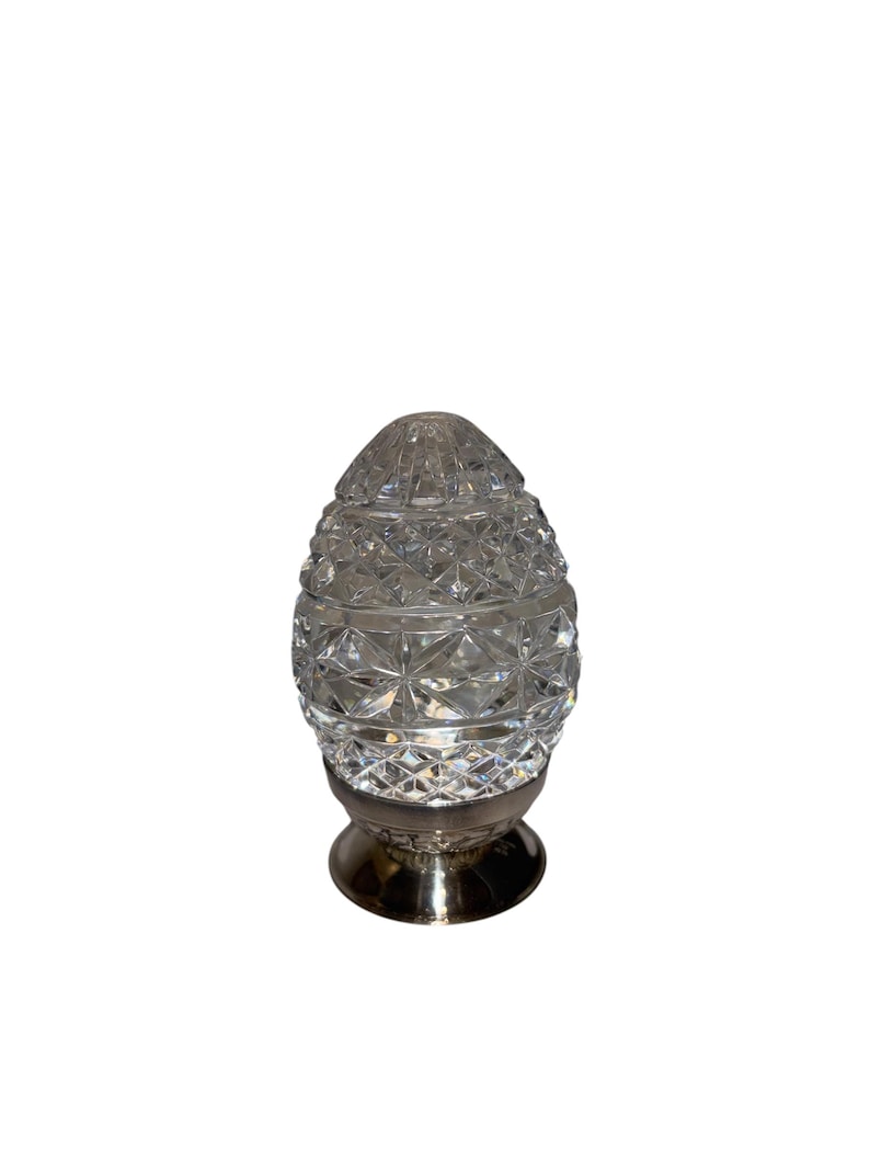 K&ouml;nnte beinhalten: Ein klarer, facettierter, dekorativer, eif&ouml;rmiger Gegenstand aus Glas mit silberfarbenem Sockel. Das Glas hat ein rautenf&ouml;rmiges Muster, und der Sockel ist rund. Die Oberseite des Eies ist ebenfalls aus Glas und facettiert. Wahrscheinlich ein Dekorationsartikel.